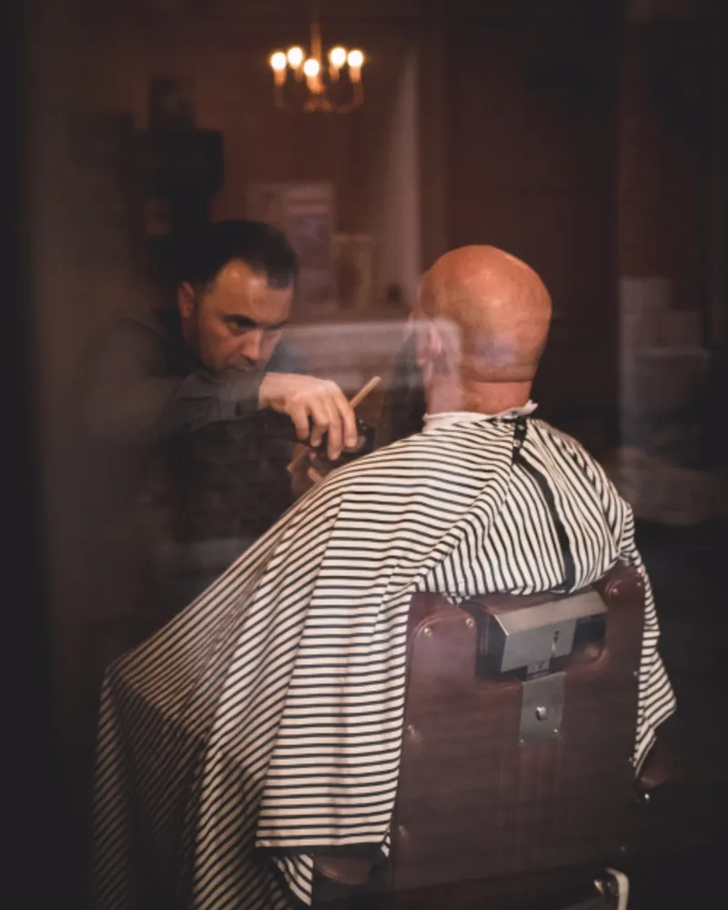 Barbeiro atendendo cliente em frente à vitrine da barbearia